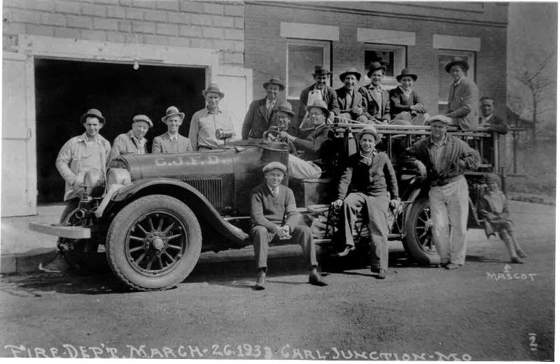 photo of men sitting on old car that work for the fire department